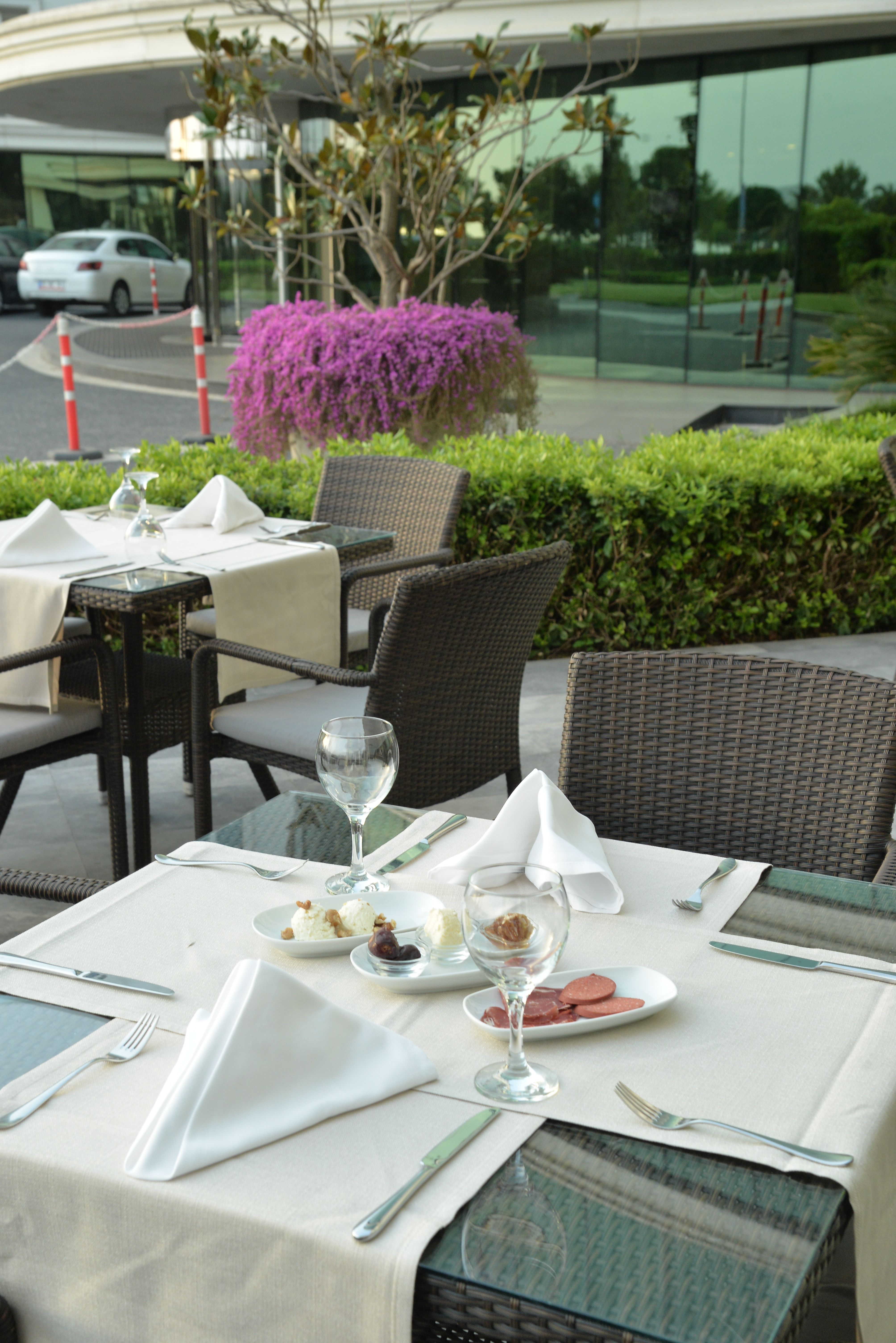 An outdoor dining table is set with white linens, silverware, and a wine glass.