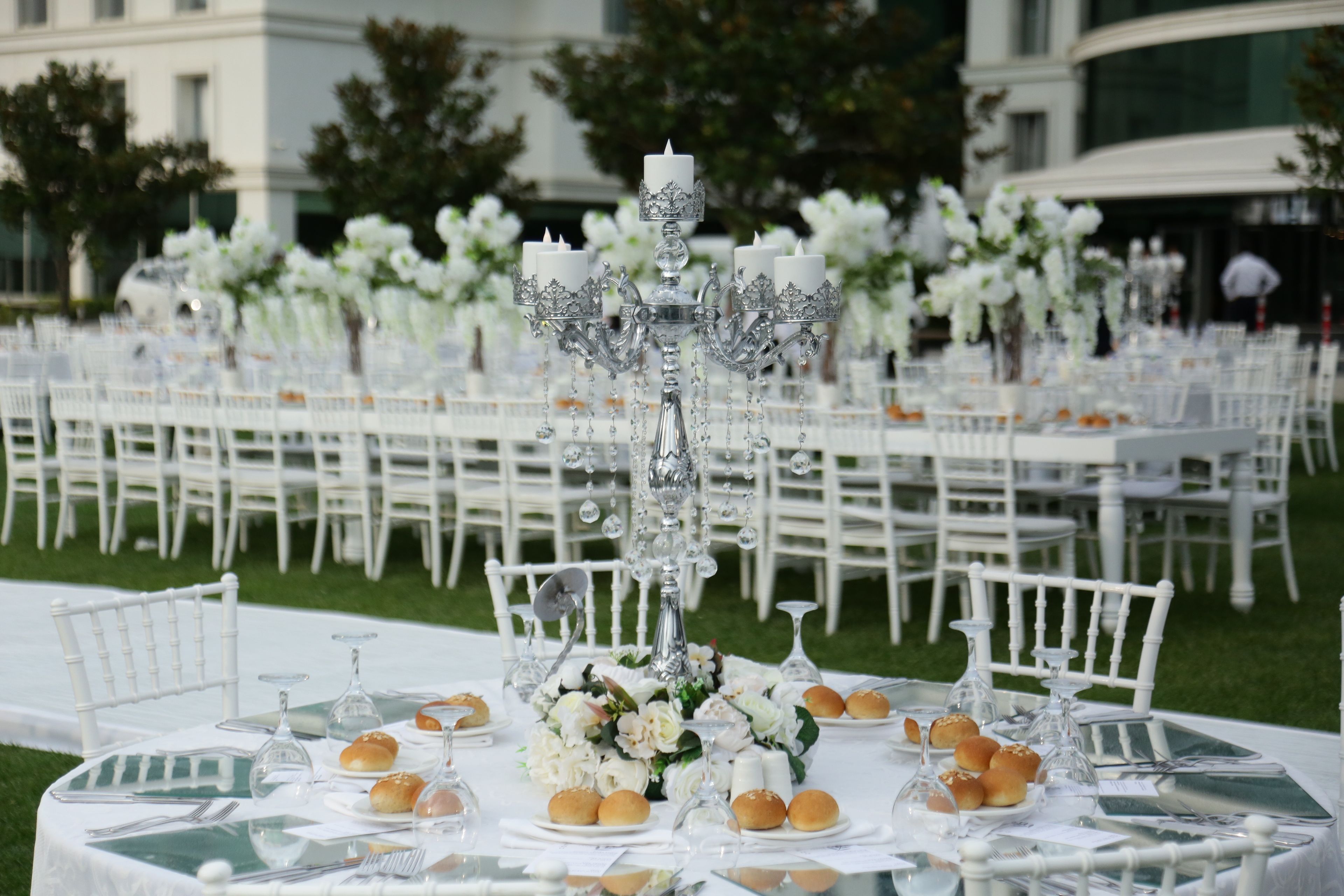 Outdoor wedding reception with long white tables, elegant floral arrangements, and silver candelabras.