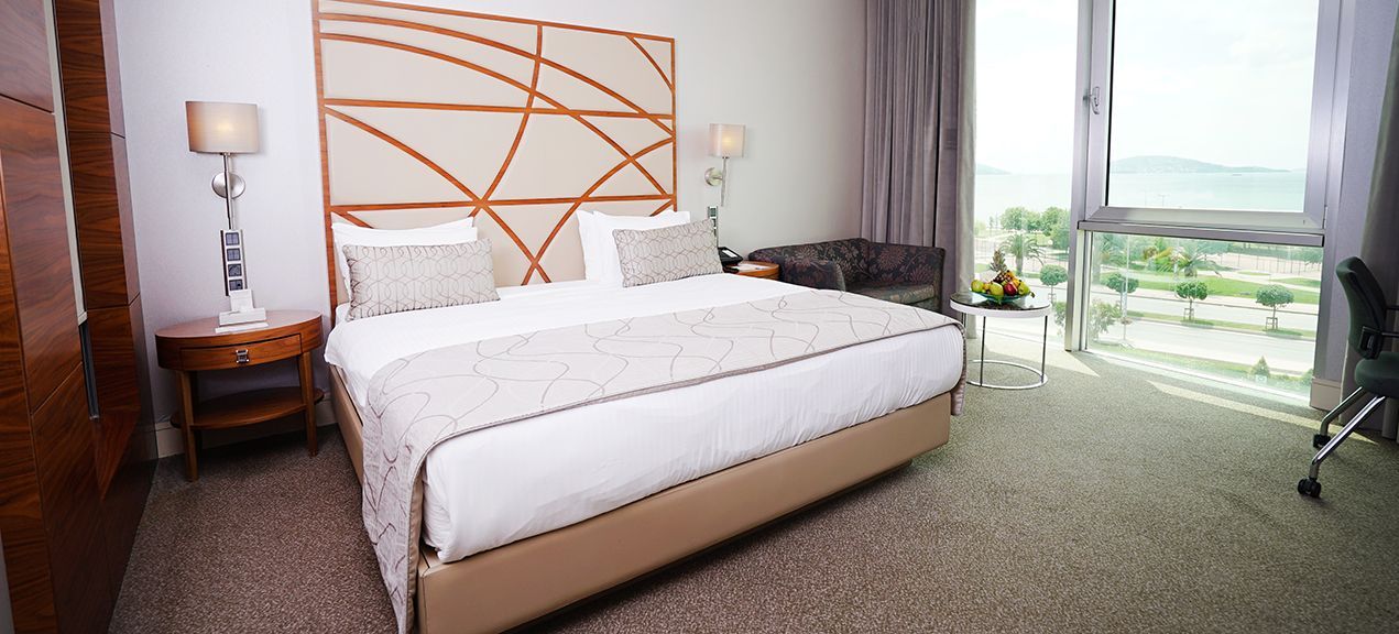 Modern hotel bedroom with a king-size bed, large window, desk, and a scenic view.