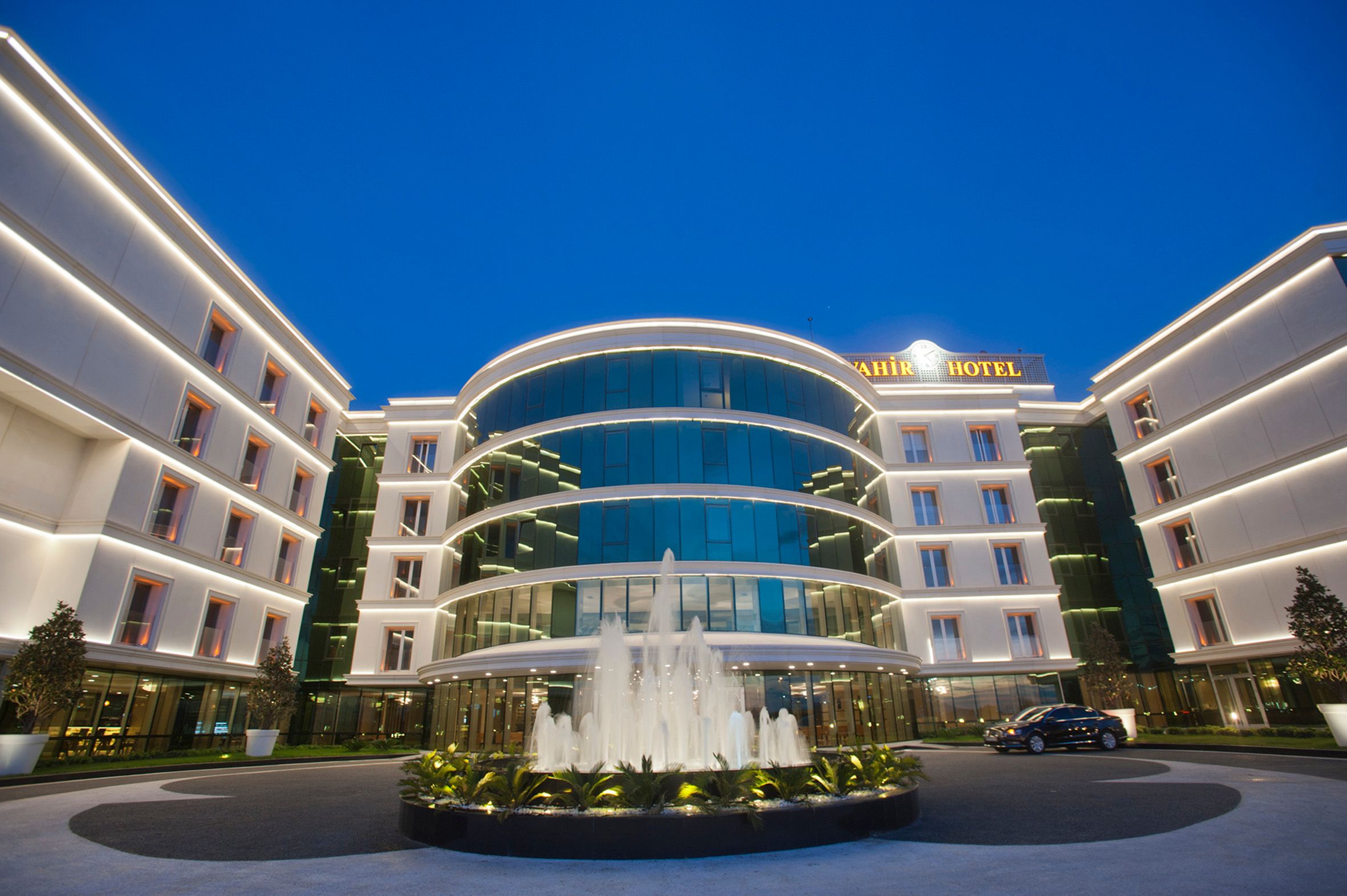 Modern hotel facade with illuminated exterior and a central glass-enclosed atrium featuring a fountain.