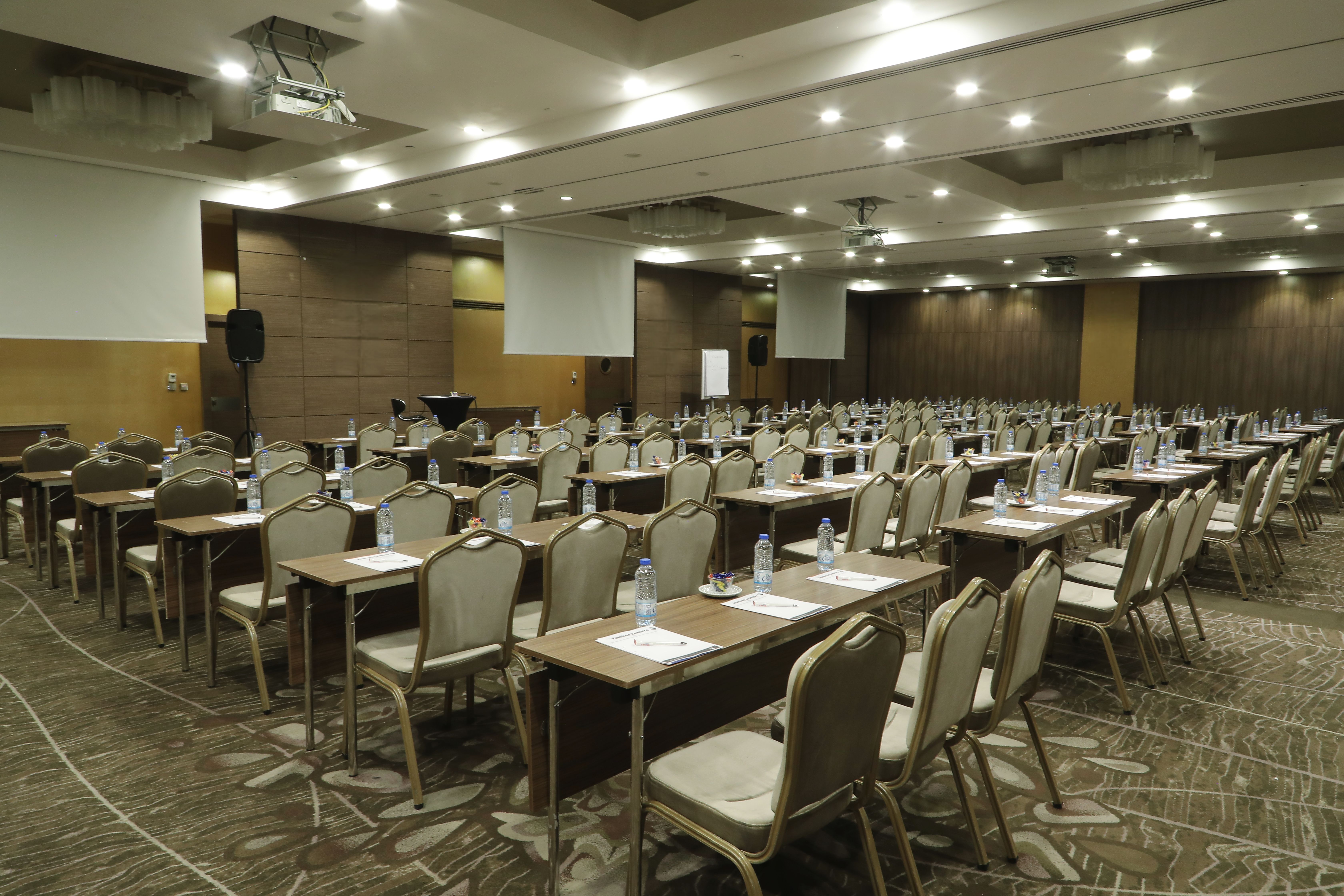 Large, empty conference room set up with numerous tables, chairs, and projector screens.