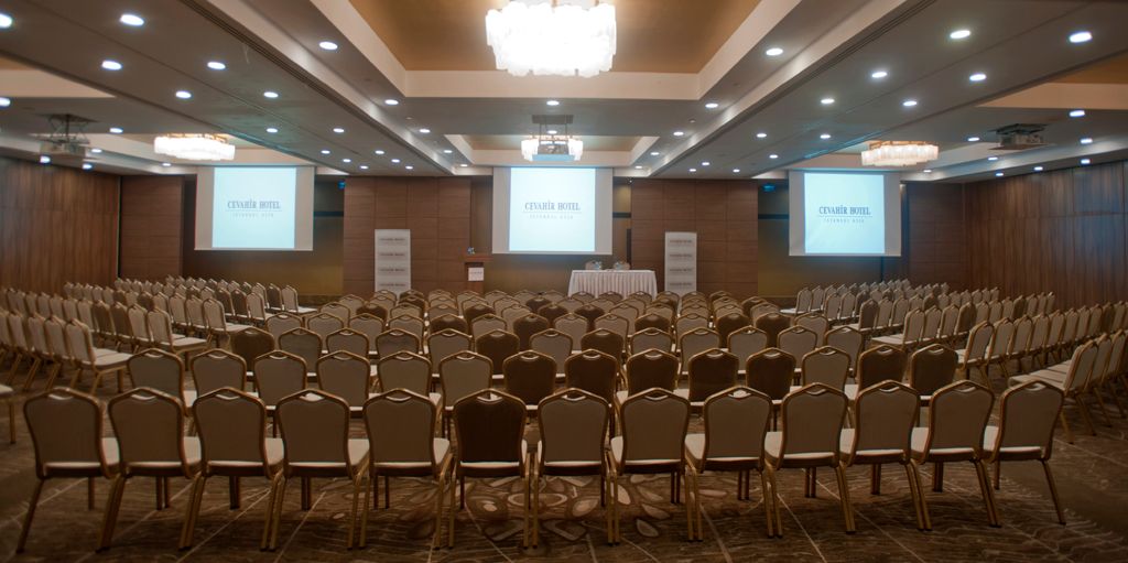 An empty, large conference room with rows of chairs facing three projection screens.