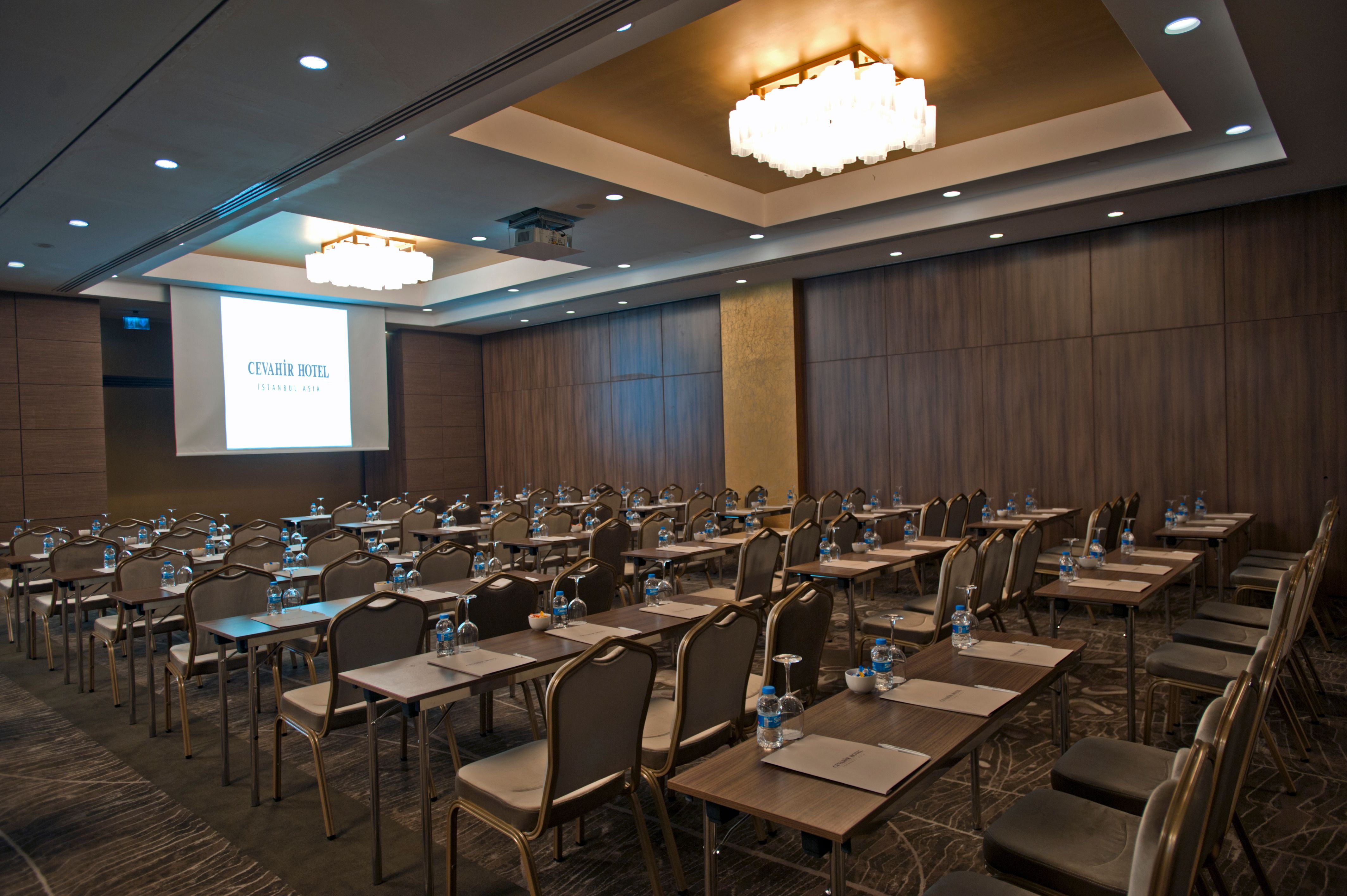 Large conference room with many tables and chairs facing a bright projector screen.