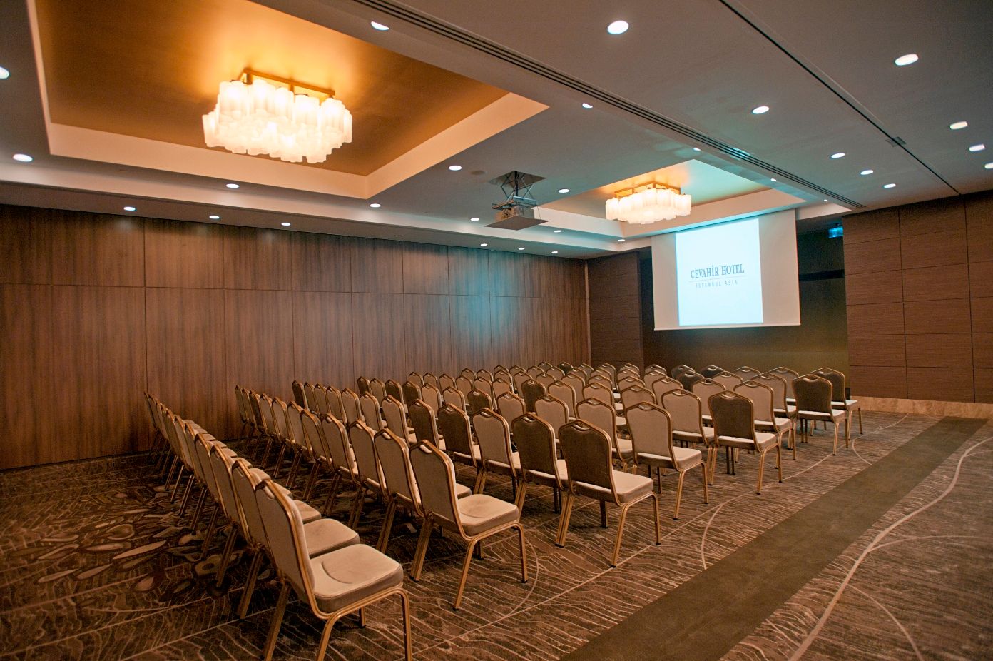 Spacious conference room with rows of empty chairs and a projection screen.